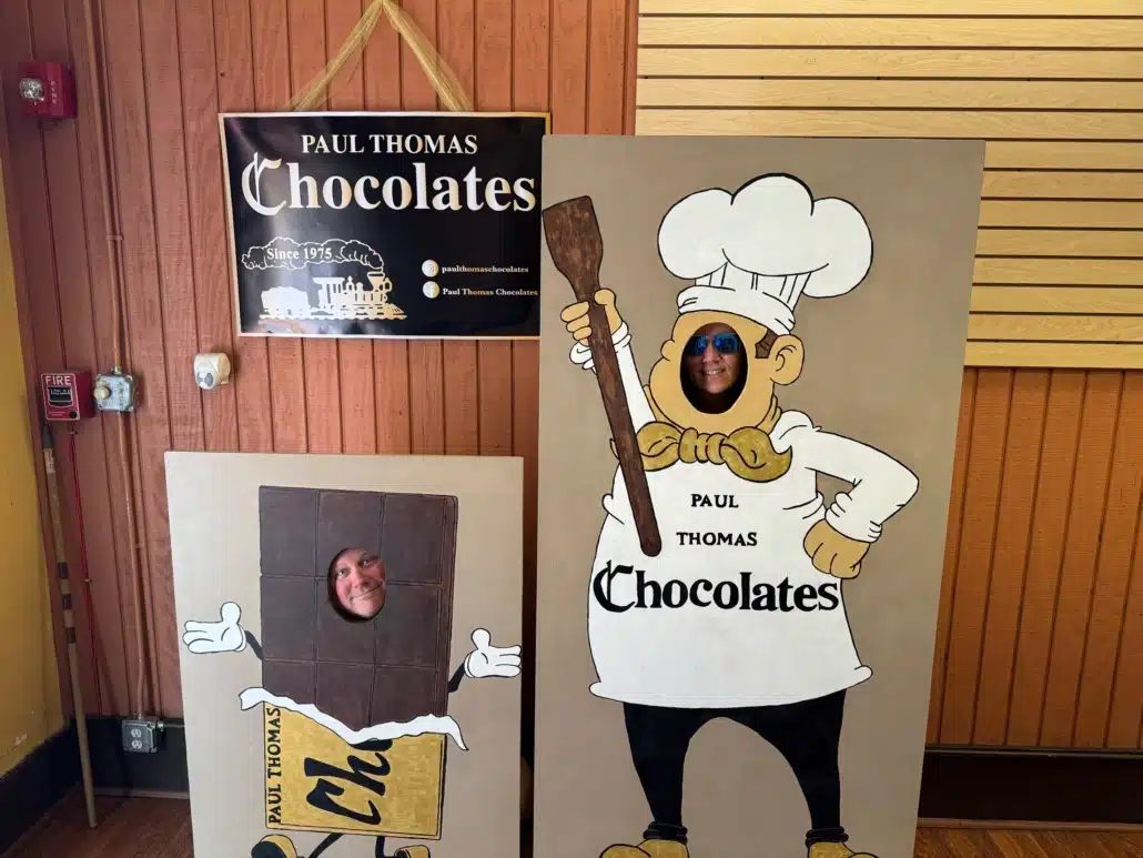 Two colleagues posing behind chocolate factory face-in-hole boards during a team outing.