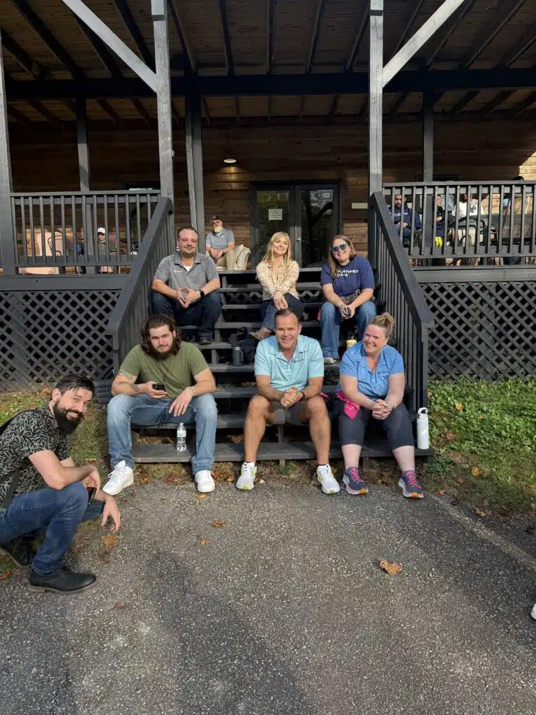 Colleagues sitting on the steps of a wooden lodge porch at a company retreat.