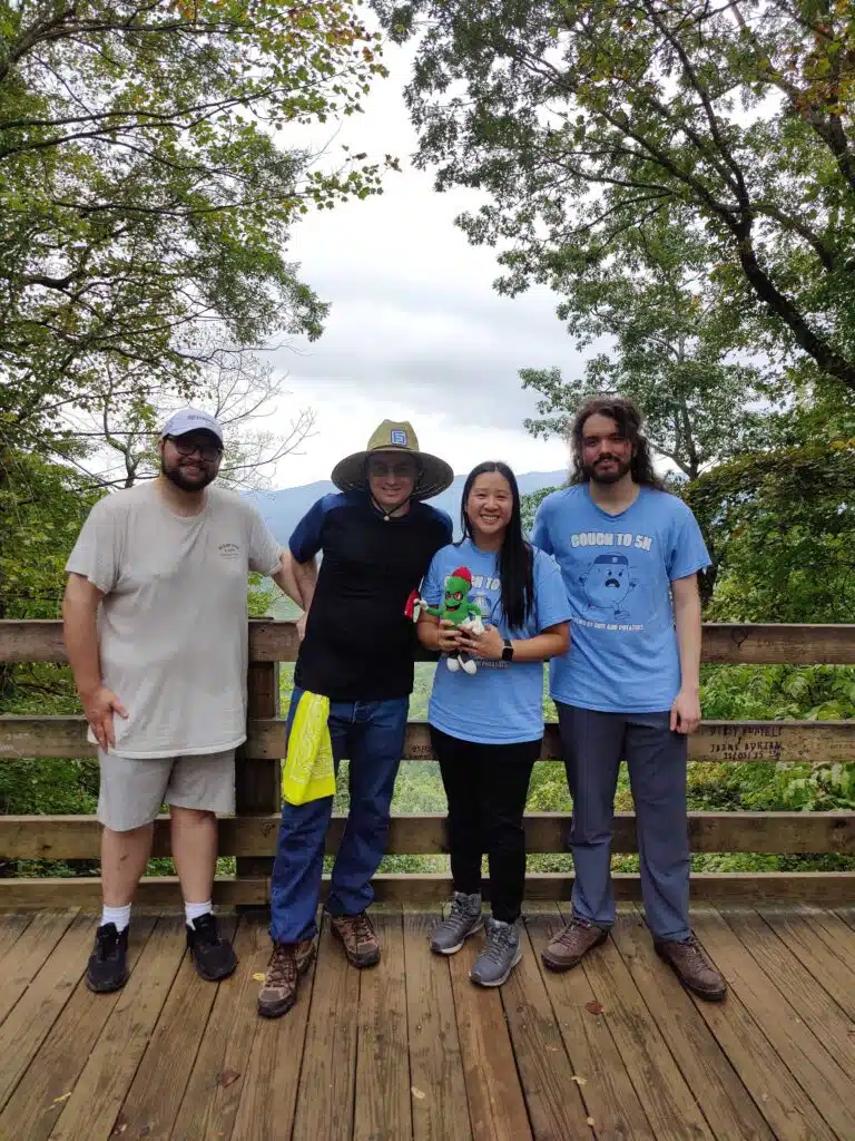 Four colleagues standing at a wooden overlook railing with a wooded mountain ridge behind them.