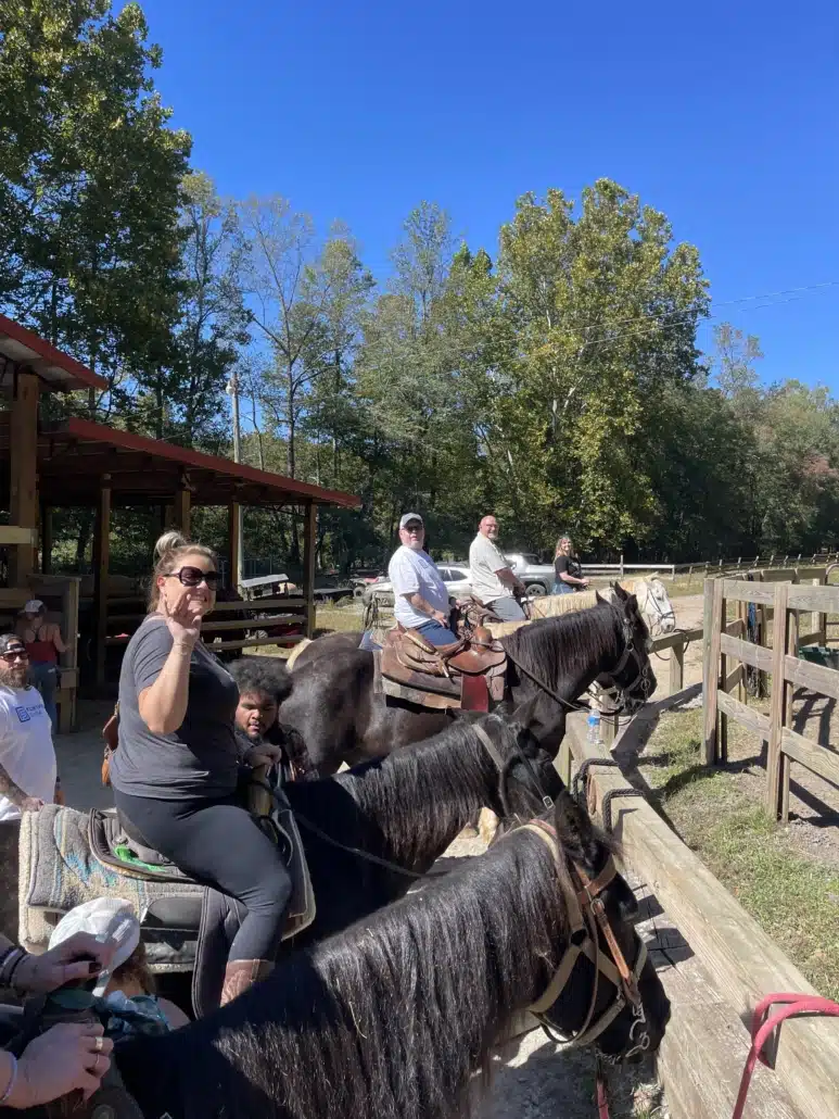 Colleagues on horseback at a trail riding stable under a clear blue sky.