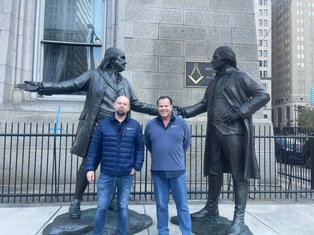 Two colleagues standing between a pair of bronze statues outside a stone civic building on a conference trip.