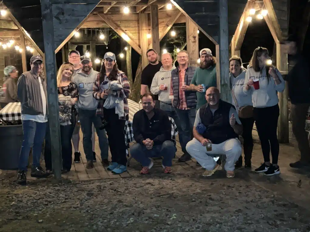 A large group posing under festoon lights in an open-sided timber shelter at night.