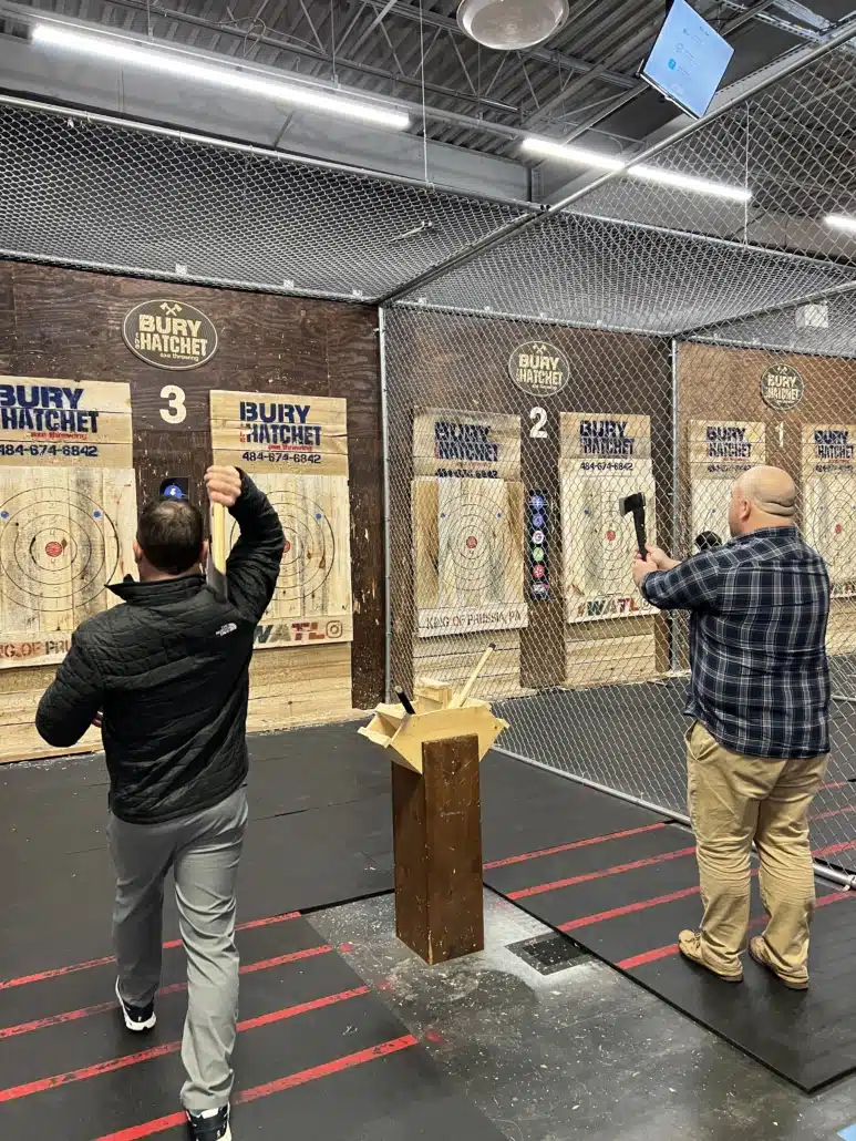 Two colleagues throwing axes at wooden targets in an indoor axe-throwing venue.