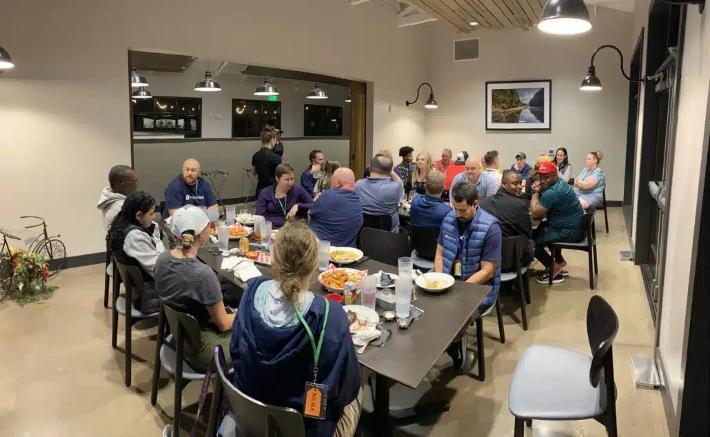 Colleagues eating together at long tables in a lodge dining room during a company retreat.